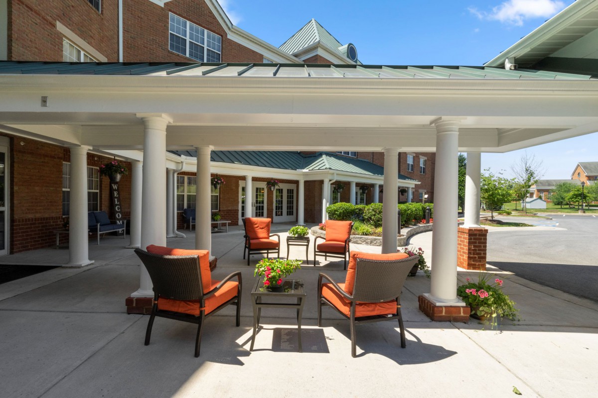 An outdoor patio area with comfortable seating, surrounded by garden and architectural columns.