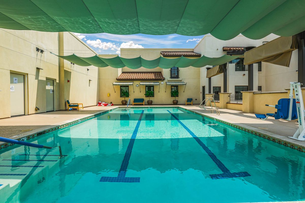 An outdoor swimming pool with shade structures and surrounding buildings.