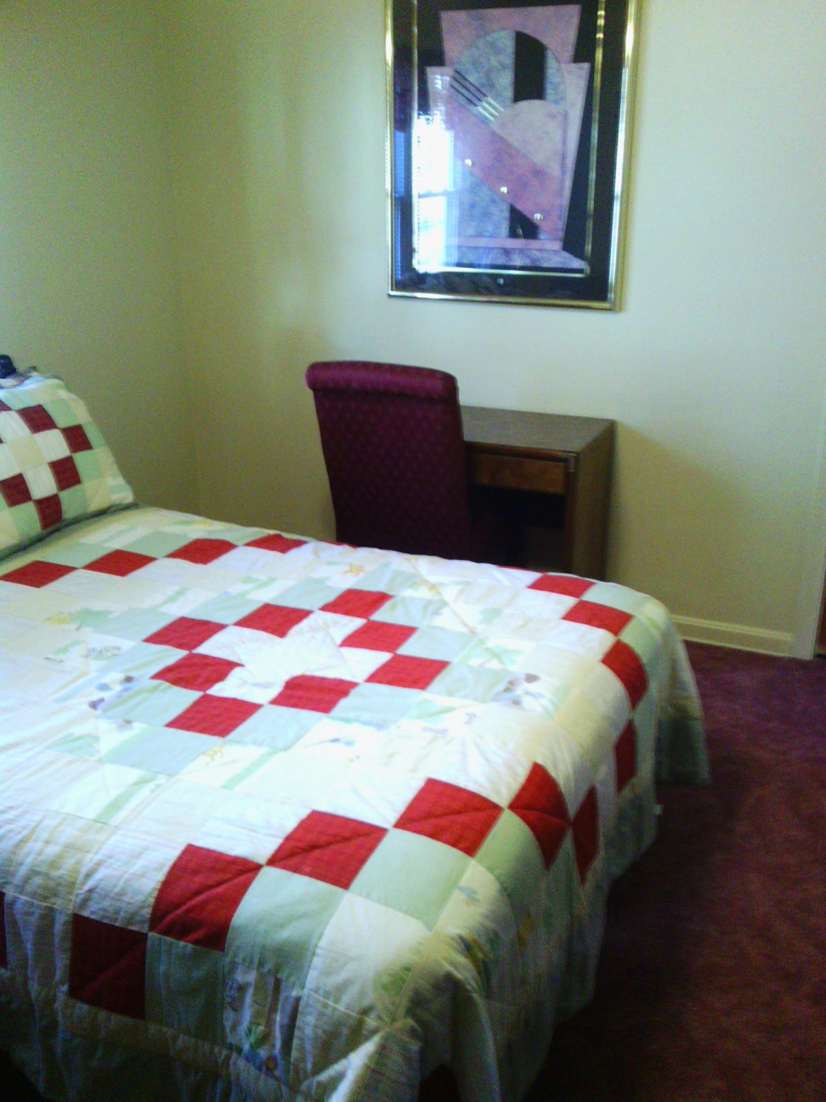 A cozy bedroom featuring a quilt-covered bed and a simple desk with a chair.