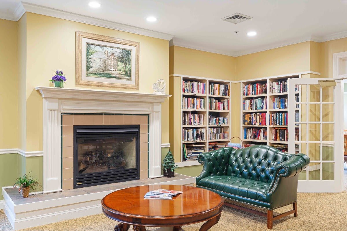 A cozy reading nook with a fireplace, green leather couch, and bookshelves filled with books.