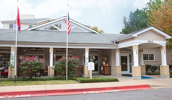 The image shows the entrance of a building with an American flag, surrounded by trees and shrubs.