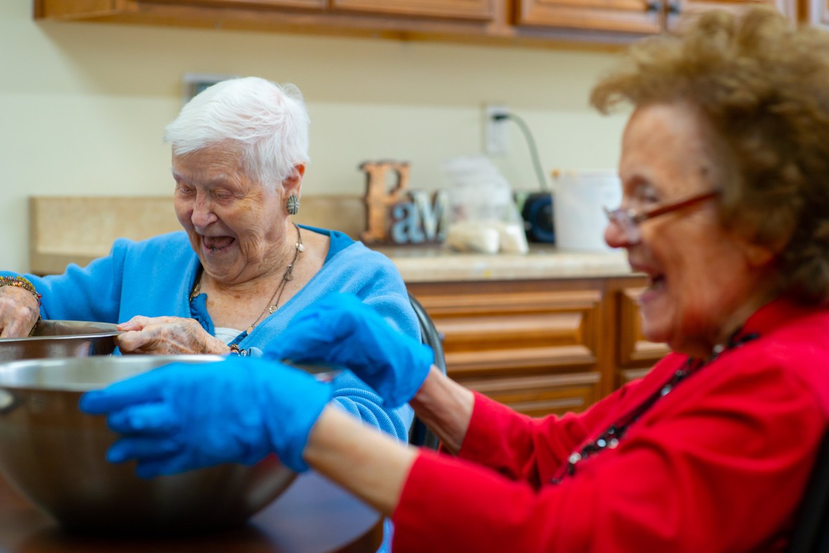 Two seniors enjoying a fun activity together in the kitchen.