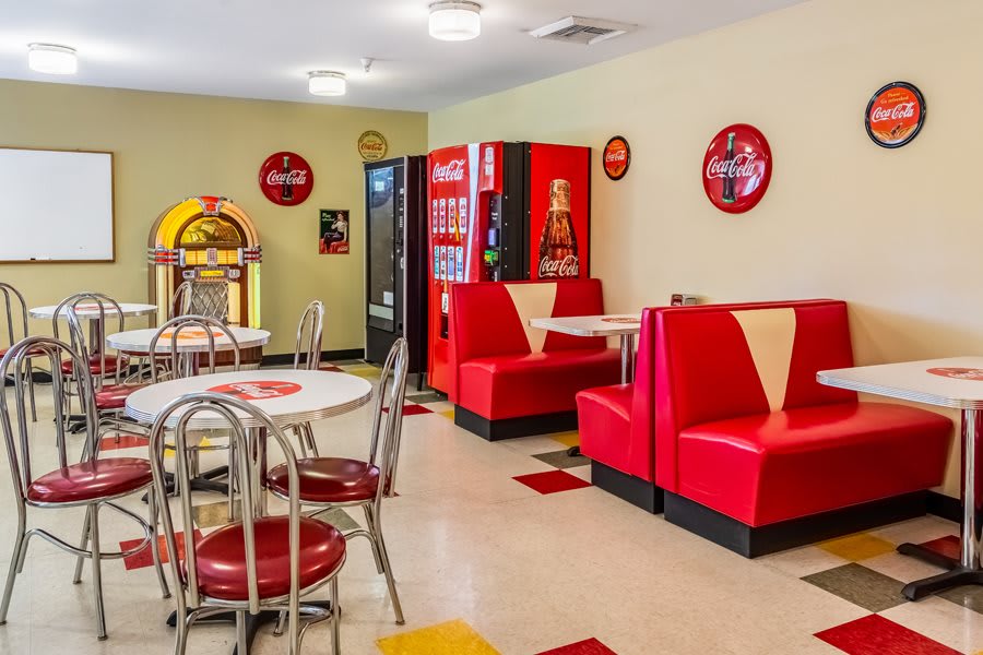 A retro diner with red booths, a jukebox, and Coca-Cola vending machines.
