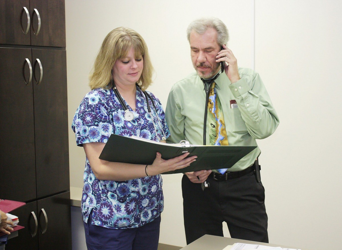 Two coworkers having a discussion; one is holding a clipboard while the other is on the phone.