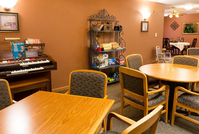 A cozy community room with tables, chairs, and a variety of games on shelves.