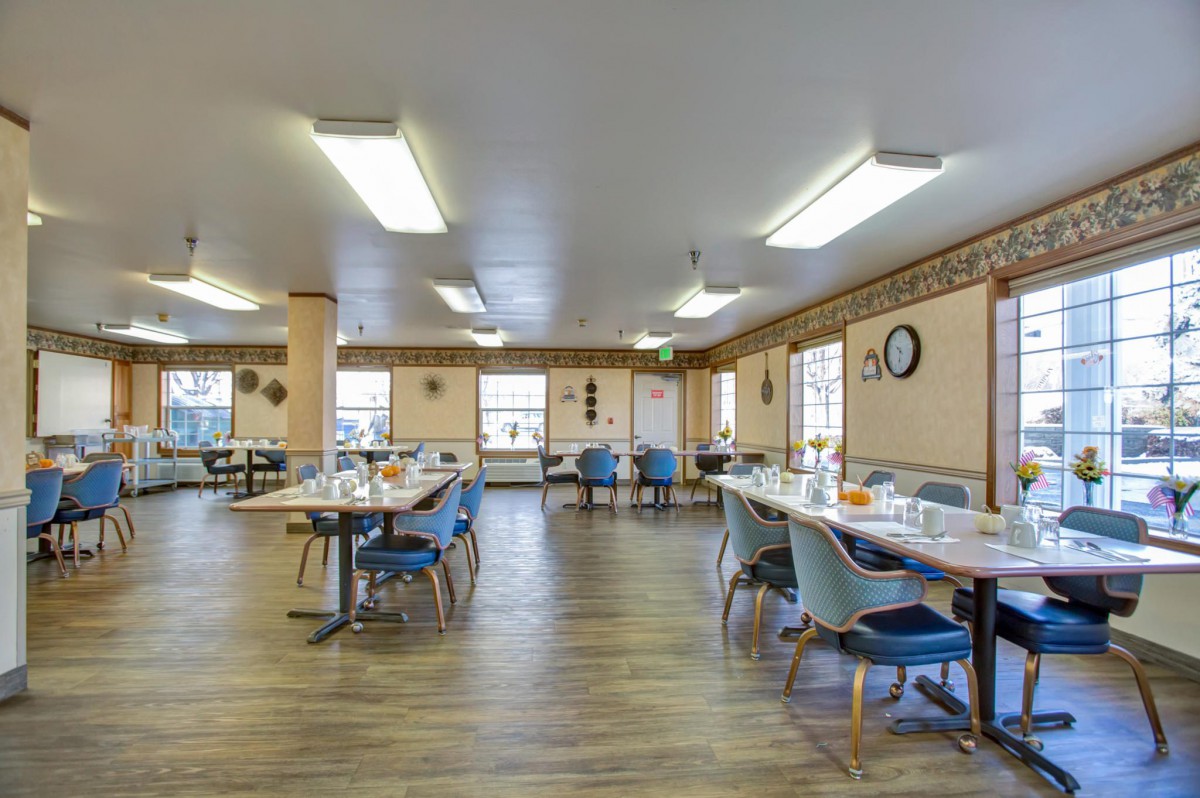 A spacious dining hall with neatly arranged tables and chairs, featuring ample lighting and large windows.