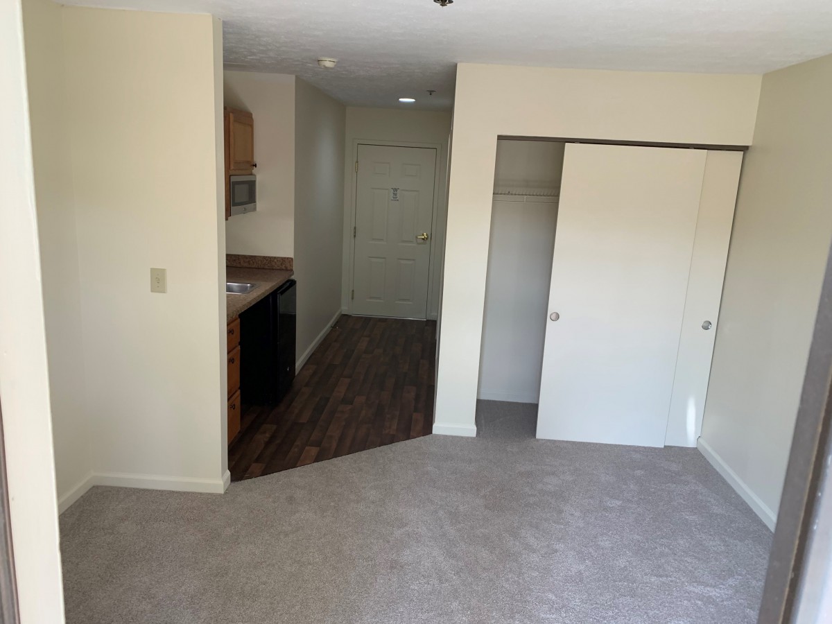 An empty apartment room with a kitchenette and closet space.