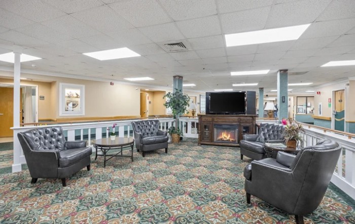 A cozy lobby with armchairs, a coffee table, and a fireplace near a television.