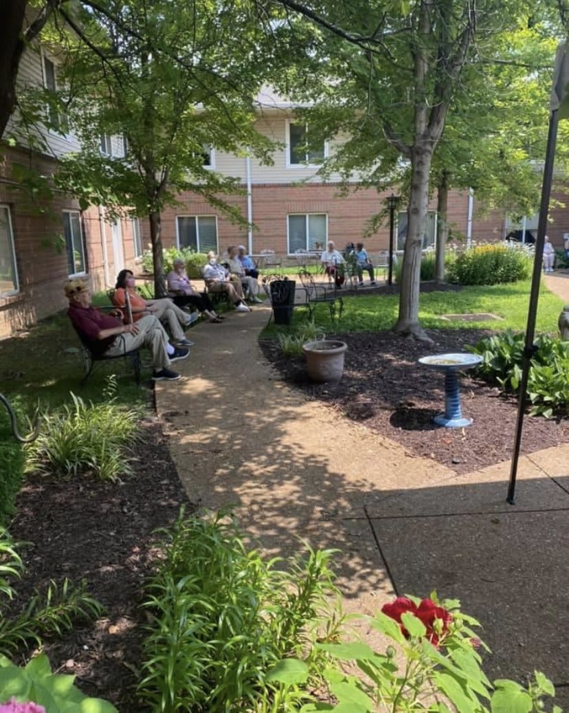 A serene garden setting with people relaxing on benches along a tree-lined pathway.