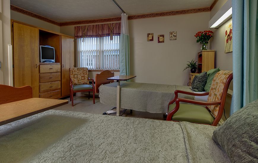 A hospital room with two beds, a television, and seating area.