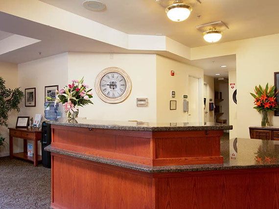 A reception desk with a wall clock and flower arrangement in an office interior.