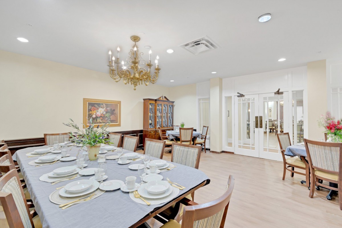 An elegantly decorated dining room featuring a large table set for a meal under a grand chandelier.