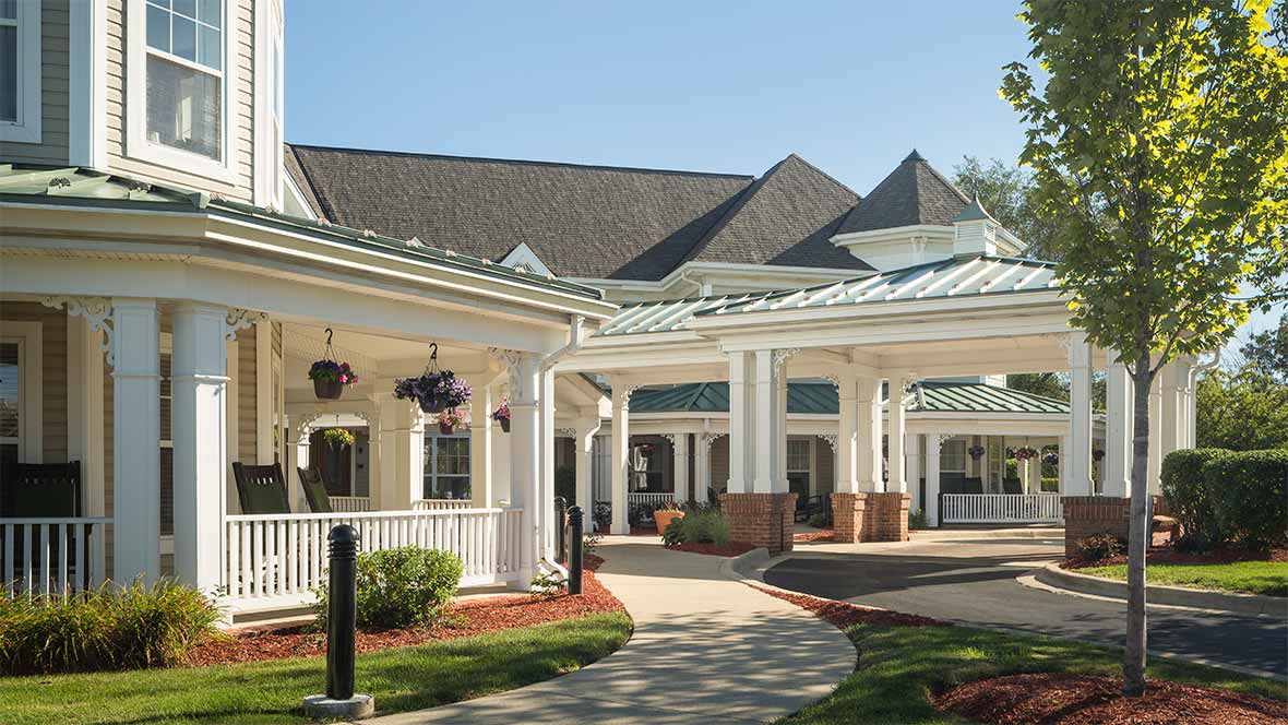 The image shows a building with a covered entrance, featuring columns and well-maintained landscaping.