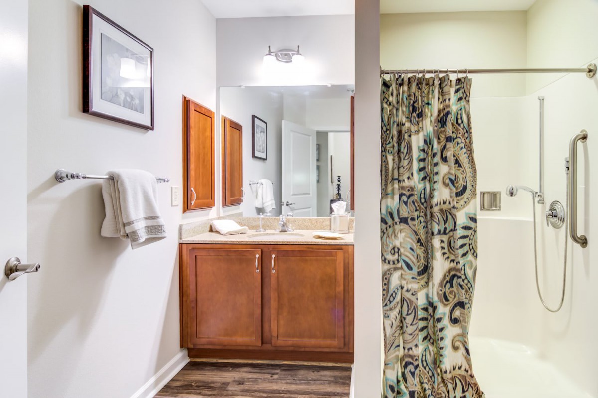 A well-organized bathroom with a wooden vanity, large mirror, and patterned shower curtain.