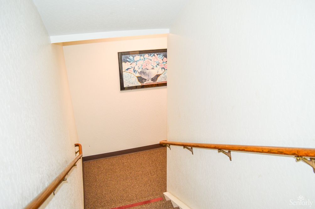 A well-lit indoor staircase with wooden handrails and a painting on the wall.