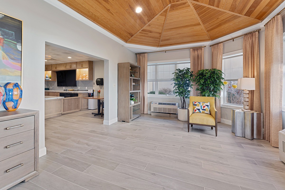 A modern open-plan living area featuring a wooden ceiling, connected kitchen, and large windows with natural lighting.