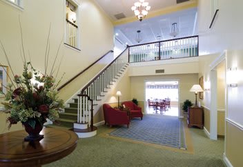 A well-lit lobby featuring a grand staircase, comfortable armchairs, and elegant decor.