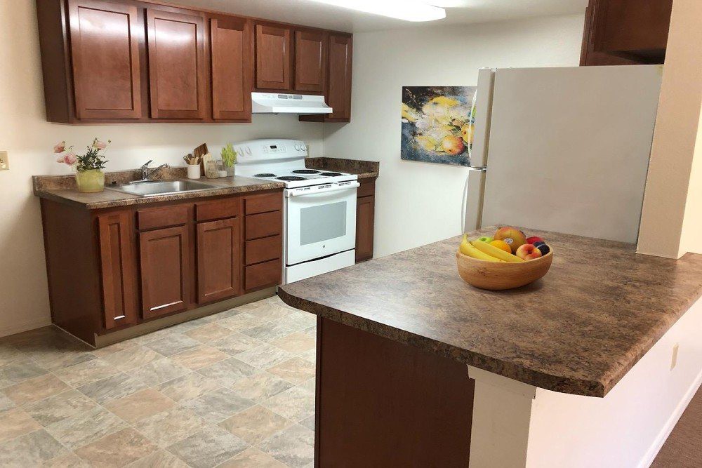 A kitchen with wooden cabinets, a stove, refrigerator, and a countertop featuring a fruit bowl.