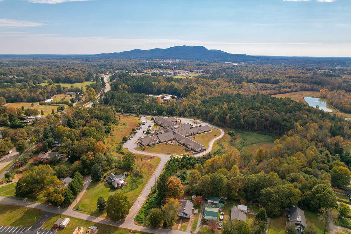 Aerial view of a residential area surrounded by forests and countryside with mountains in the distance.