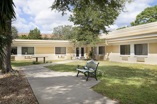 A serene outdoor area featuring a building, pathways, and a bench surrounded by greenery.