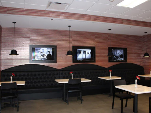 A modern restaurant interior featuring booth seating and wall-mounted TVs.