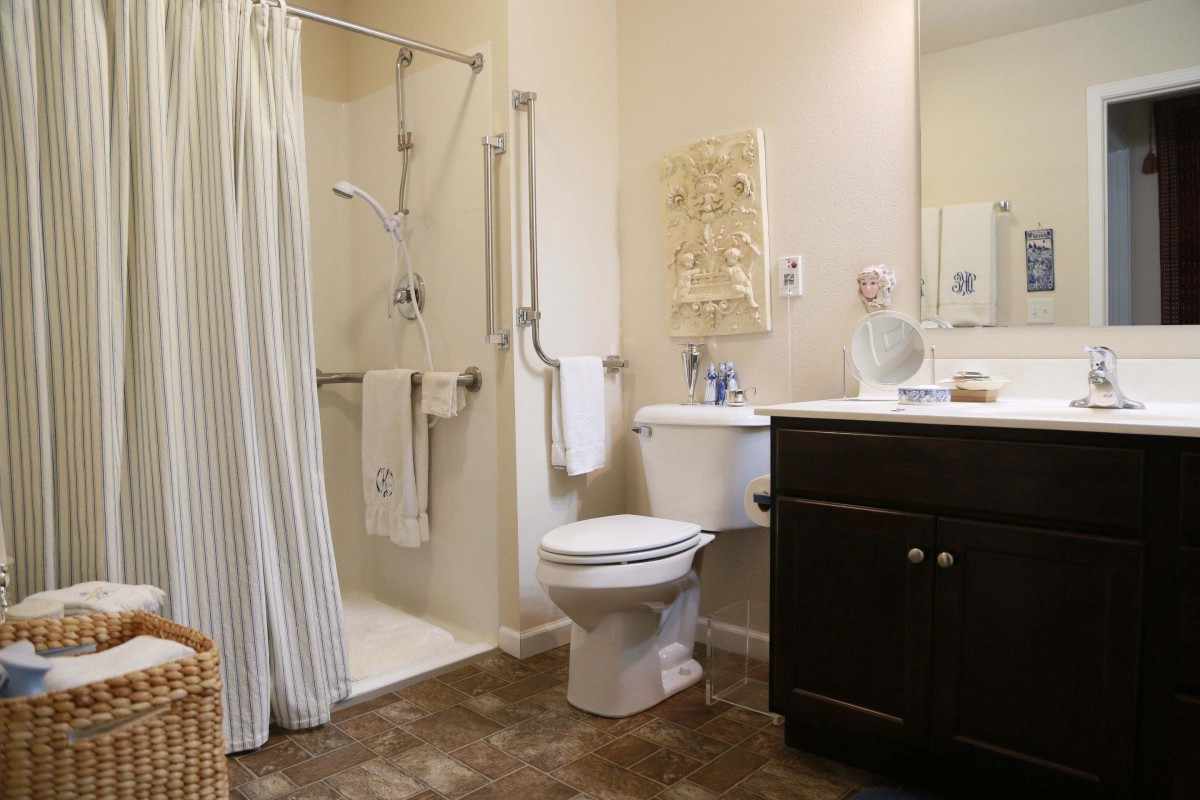 An accessible bathroom with a shower, toilet, and sink featuring grab bars for safety.
