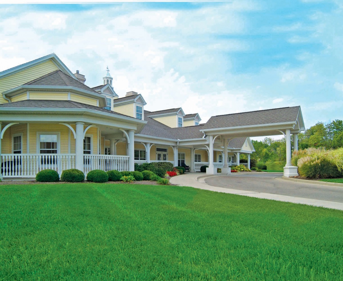A large yellow residential building with a porch and well-maintained lawn under a blue sky.