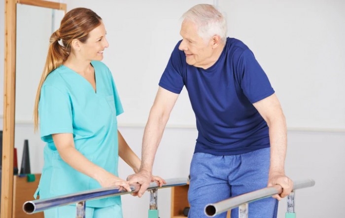 A nurse assists an elderly man with walking exercises in a rehabilitation setting.