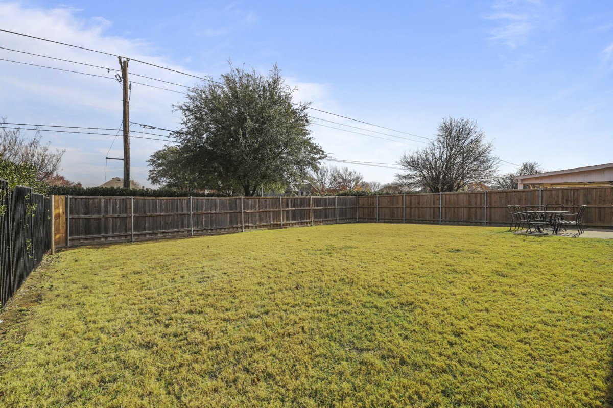 A spacious backyard with a fenced perimeter and green lawn under a clear blue sky.