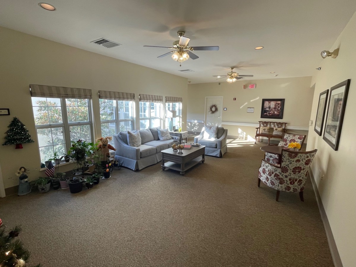 A spacious and well-lit living room with comfortable seating, large windows, and ceiling fans.