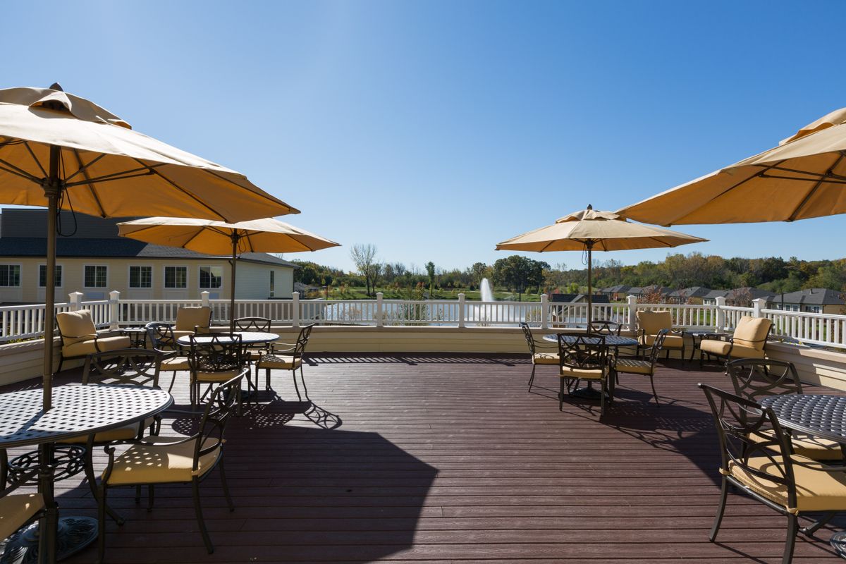 A sunny outdoor deck area with tables, chairs, and umbrellas overlooking a lake.