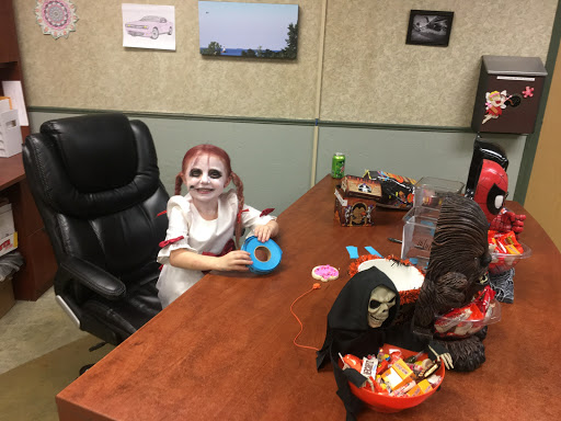 A child in Halloween costume enjoying treats at an office desk.