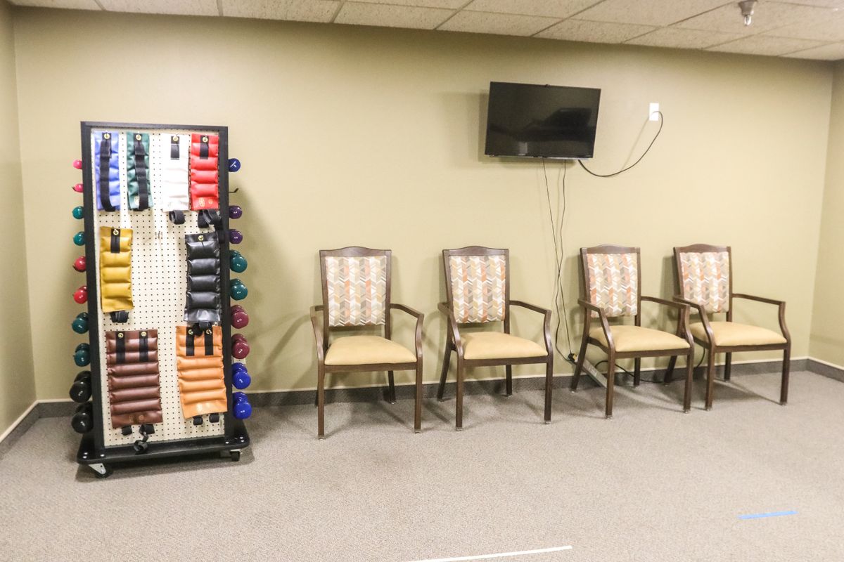 A waiting room with chairs, a wall-mounted television, and a rack of exercise bands.