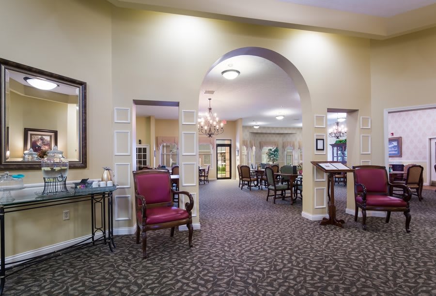 A spacious dining area with red chairs and carpeted flooring, featuring an inviting archway and soft lighting.