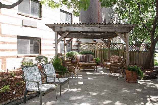 A cozy outdoor patio with chairs and a wooden gazebo, surrounded by plants.