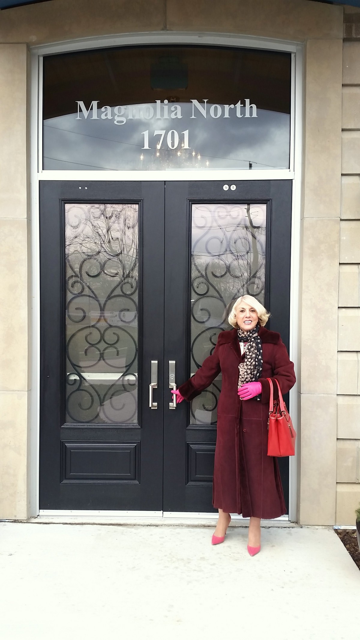 A woman in a burgundy coat stands in front of ornate double doors.