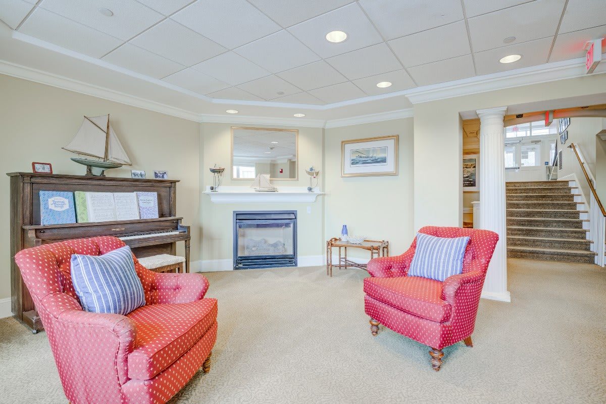 A cozy living room with a piano, fireplace, and red armchairs.