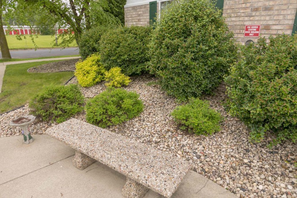 A stone bench in a landscaped garden with shrubs and pebbles.