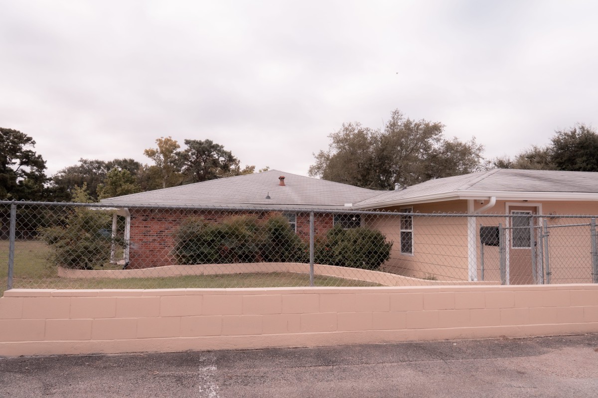 A suburban residential house with a brick wall and driveway on a cloudy day.