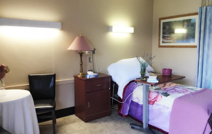 An interior view of a hospital room with a bed, nightstand, and medical equipment.