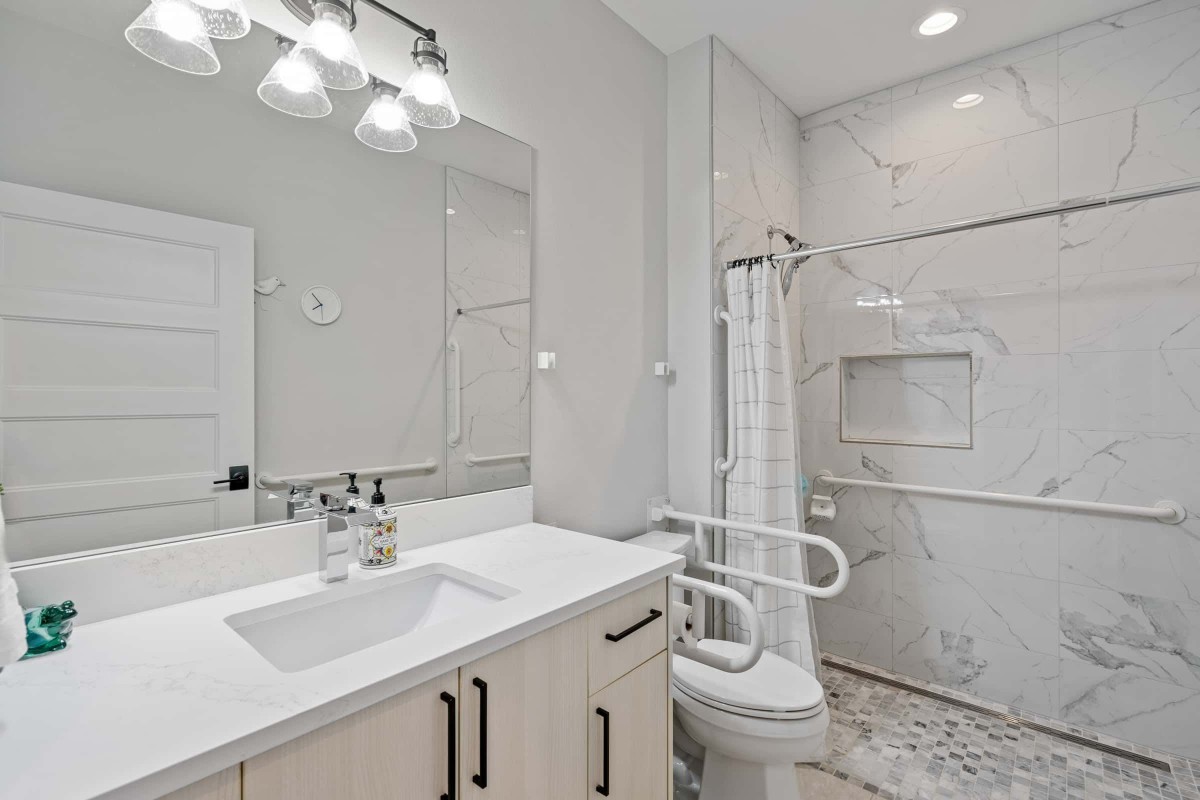 A modern, accessible bathroom featuring a shower with handrails and white interior design.