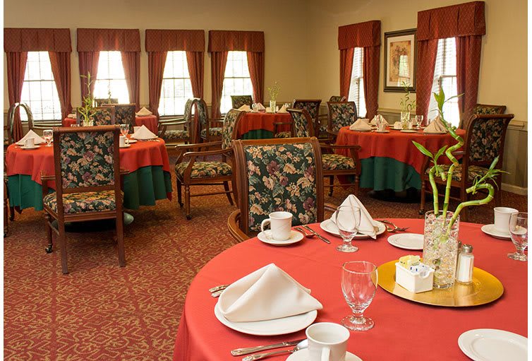 An elegantly set dining room with tables covered in red tablecloths and neatly arranged chairs.
