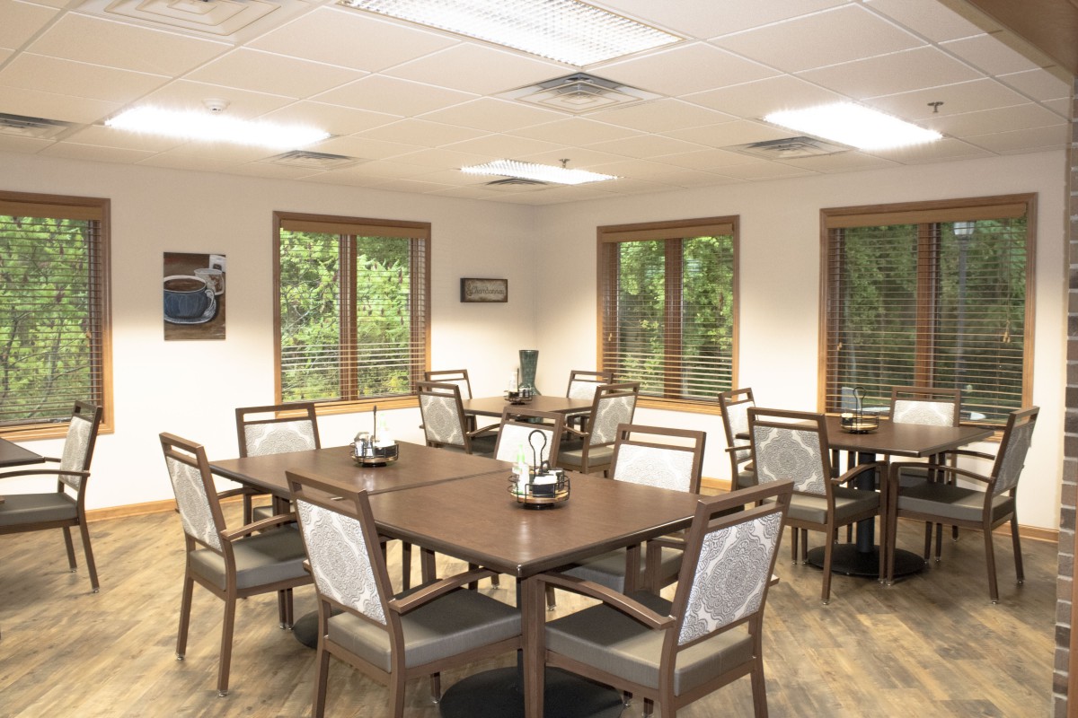 An empty dining area with several tables and chairs, lit by overhead lights and natural light from the windows.