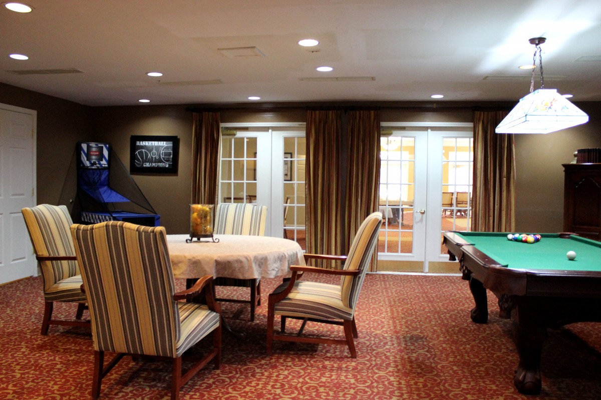 A cozy game room featuring a pool table and a round table with striped chairs.