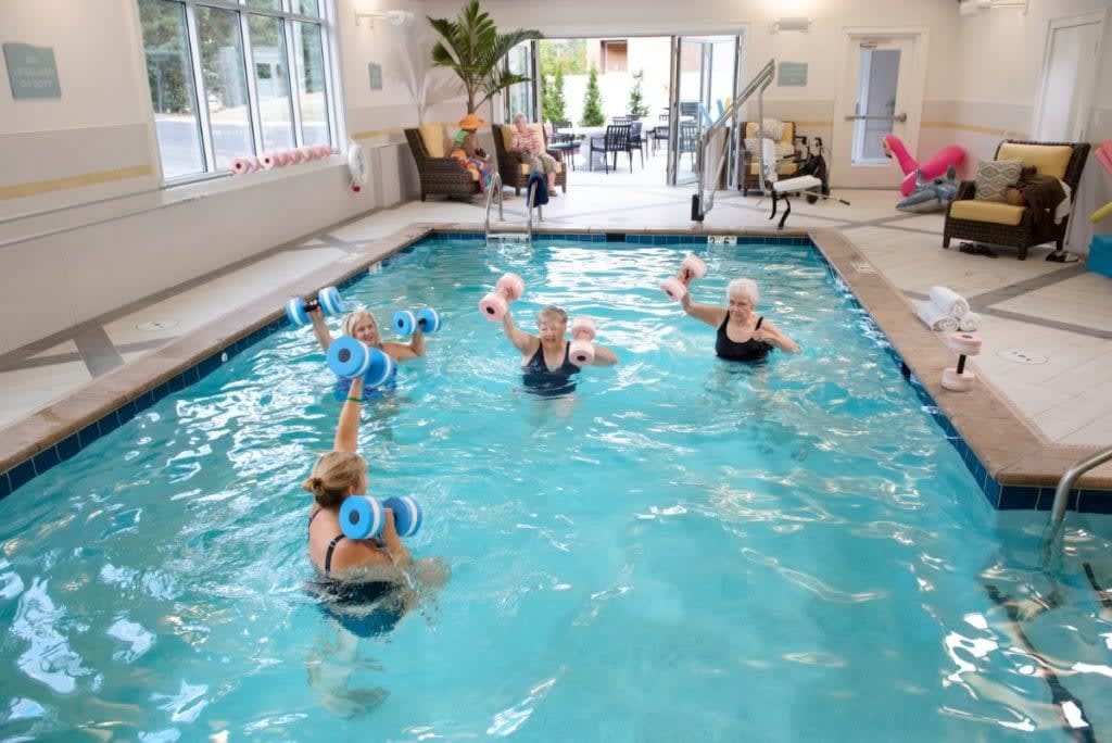 A group of seniors participating in a water aerobics class in an indoor pool.