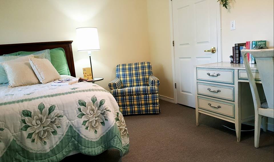 A cozy bedroom with a bed, plaid armchair, and white dresser.