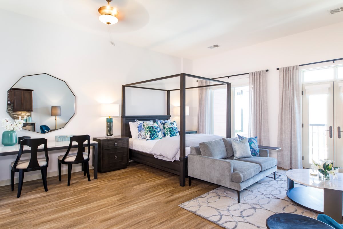 A modern bedroom featuring a canopy bed with decorative pillows, a stylish rug, and a comfortable sofa, all set on hardwood flooring.
