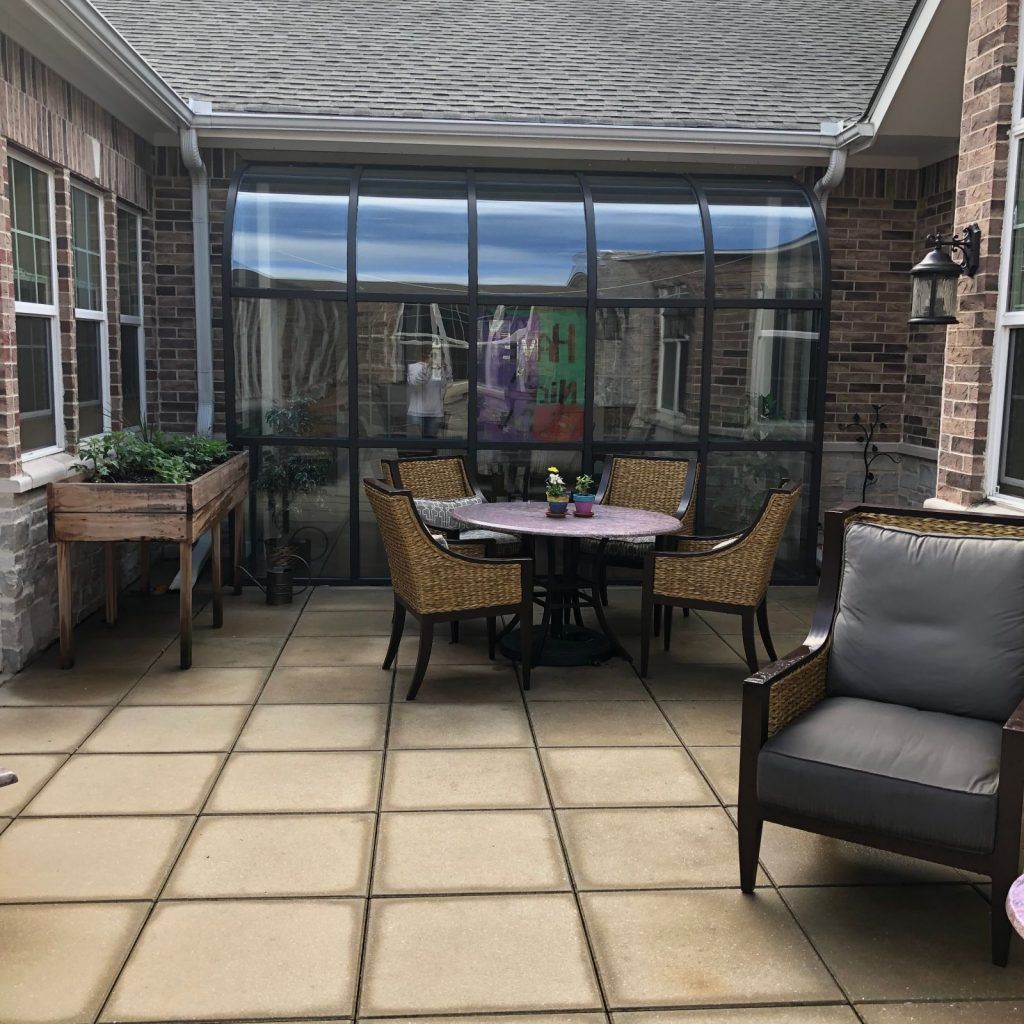 A cozy patio with a table and chairs set, featuring potted plants and a stone tile floor.