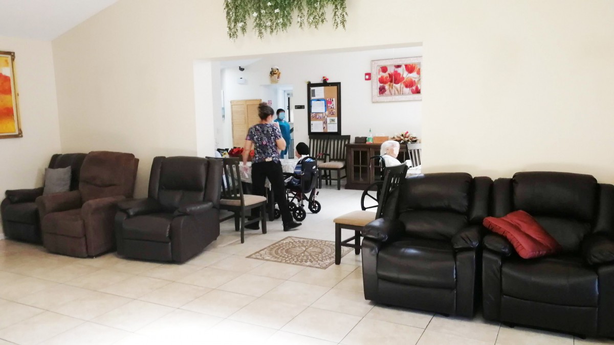 A cozy living room with leather sofas and a view into the dining area where people are gathered.