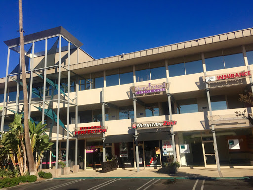A modern shopping complex featuring various storefronts under a clear blue sky.